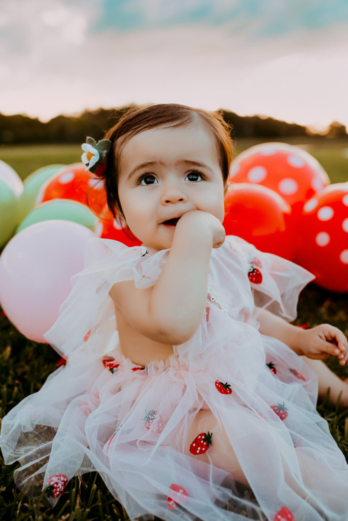 first birthday photoshoot of a toddler girl wearing strawberry themed tulle dress 