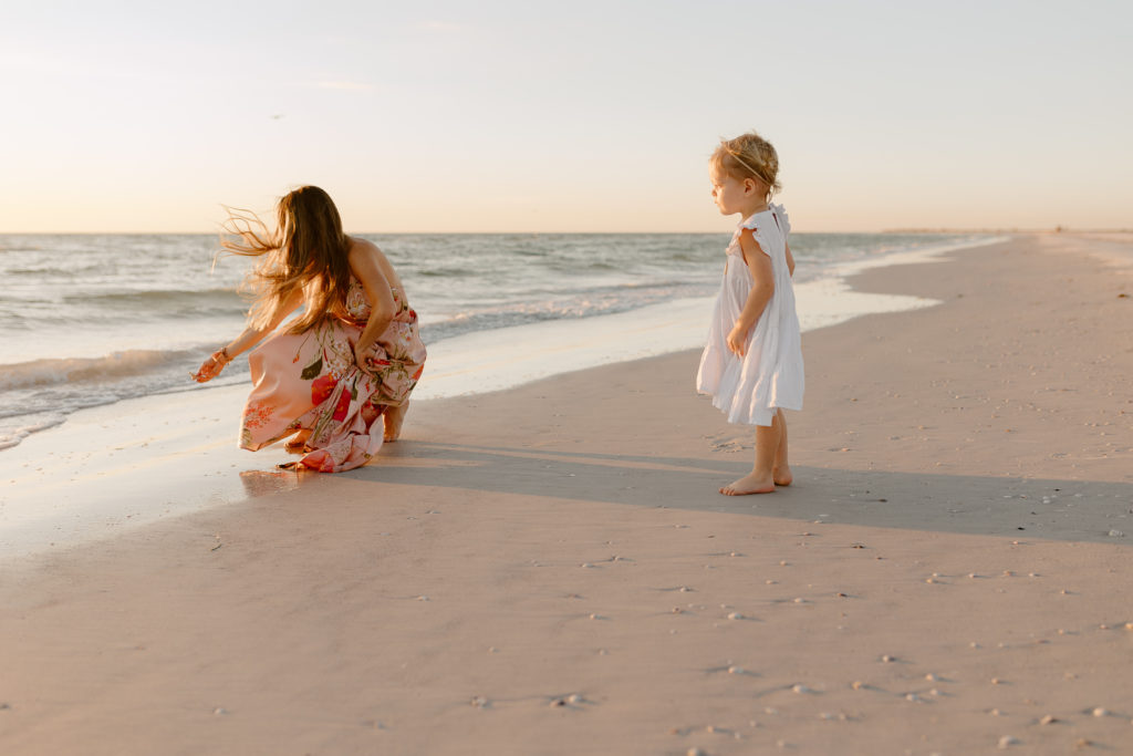 Mom and child searching for shells on the beach at sunset 