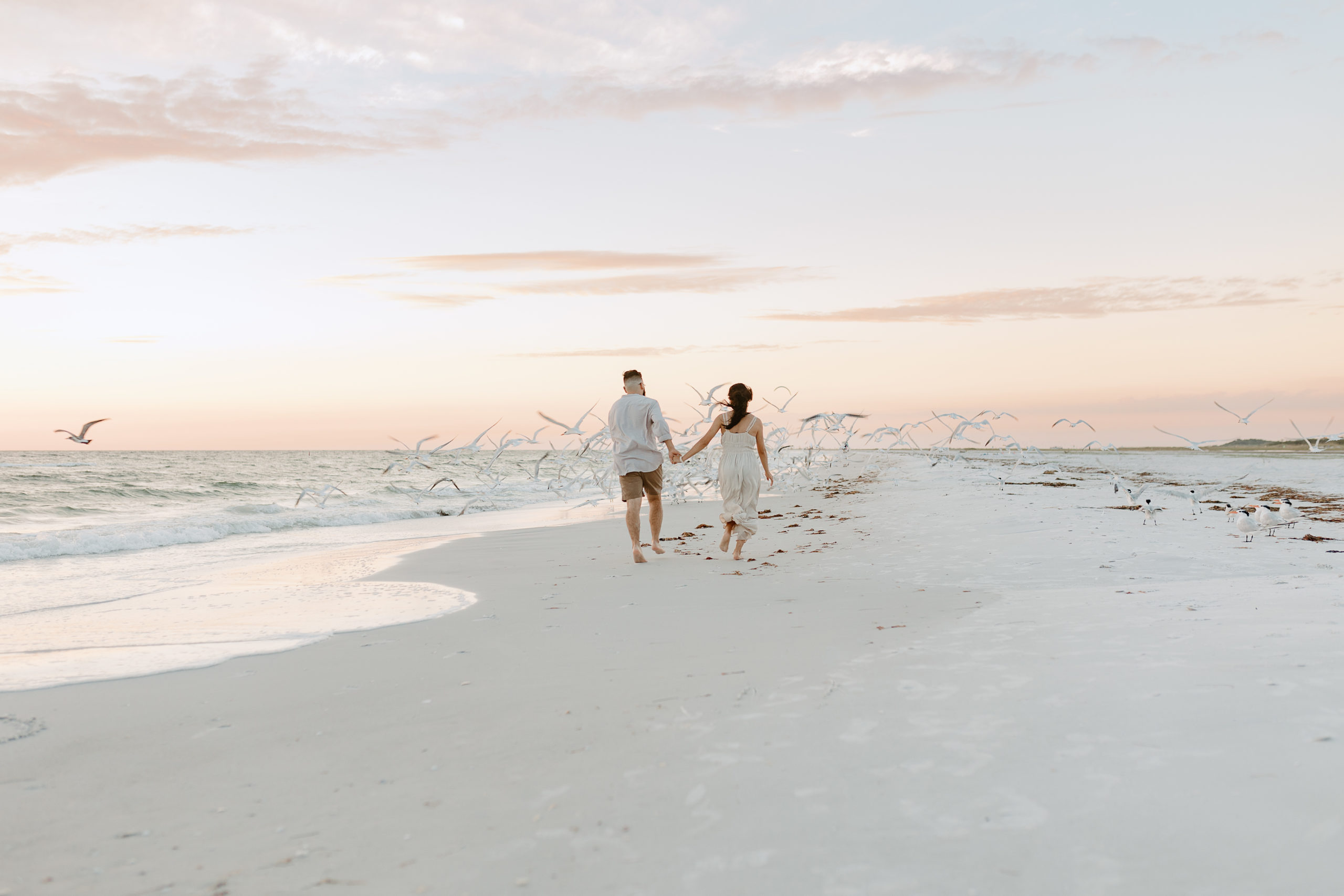 Running into the sunset with seagulls flying off in the background after an engagement during an extended family session in Treasure Island, Florida. 