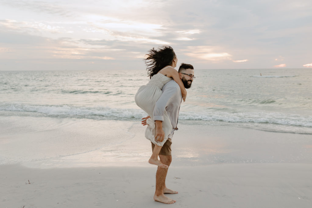 Piggy back rides on the beach at sunset. Couples photography by Michelle Medina Photography.