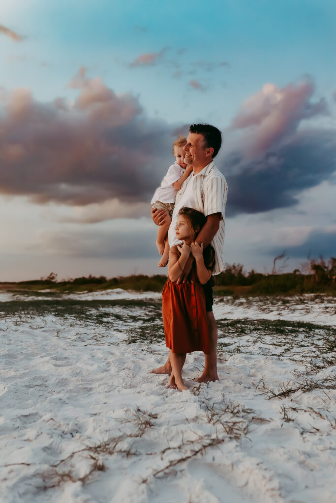 A father with his children watching the sunset during their family beach photos in Tampa. By Michelle Medina Photography.